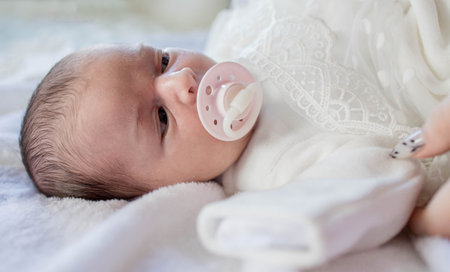 Newborn baby lying with baby pacifier covered with white blanket