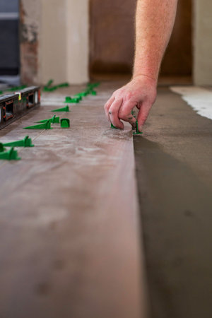Close up hands of repairman laying tiles with tile leveling system on the floor in a new house.