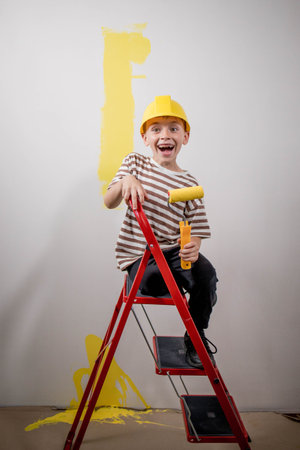 Child paints a wall with a roller. The boy is holding a large paint brush. House repairの写真素材
