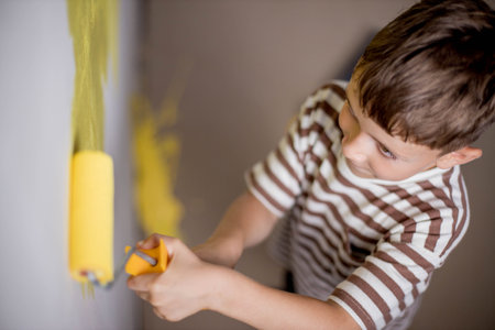Child paints a wall with a roller. The boy is holding a large paint brush. House repair.の写真素材