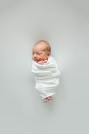 A 3-day-old baby wrapped in white cloth sleeping on a white background.の写真素材