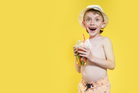Cute little boy with inflatable ring and cocktail glass on yellow background.の写真素材