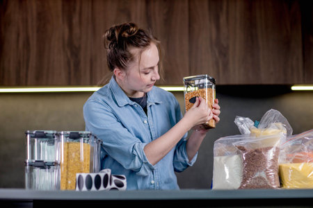 Nice woman organizes the placement of food in plastic cans. Woman signs cans of bulk food.の写真素材