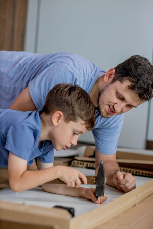 Father and son assemble new furniture on floor of new apartment, concept of experience and training
