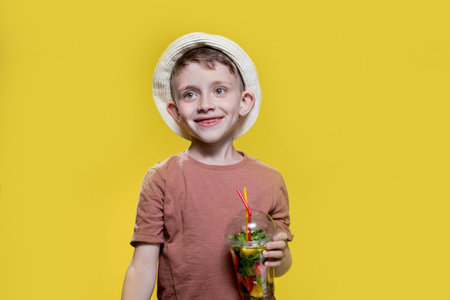 Cute little boy with inflatable ring and cocktail glass on yellow background.の写真素材