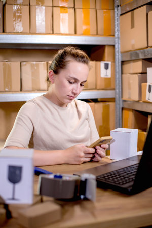 Young entrepreneur small business checking internet orders on smartphone and preparing boxed items for delivery to customers.の写真素材