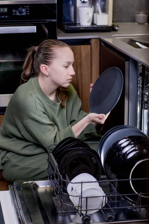 Woman unloading clean dishes from dishwasher at home.の写真素材