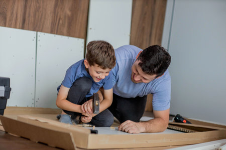 The son helps dad to collect furniture, there are tools and boards nearby. Assembling furniture at home.の写真素材