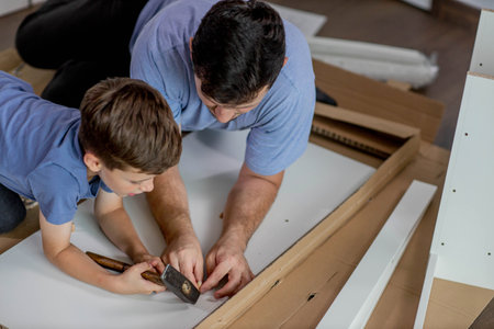 The son helps dad to collect furniture, there are tools and boards nearby. Assembling furniture at home.の写真素材