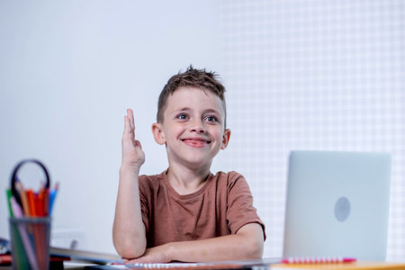 Schoolboy boy raises hand in online lesson at home.の写真素材