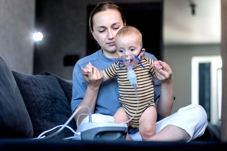 Woman with infant son makes inhalations using a nebulizer at home.の写真素材