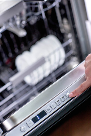 Woman's hand turns on the dishwasher to wash the dishes. Built-in appliances in the kitchenの写真素材