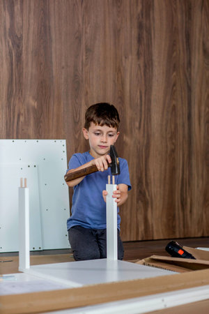 Boy hammers a wooden dowel with a hammer. Assembling furniture at home.の写真素材