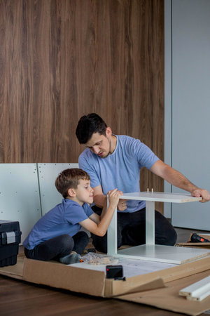 The son helps dad to collect furniture, there are tools and boards nearby. Assembling furniture at home.の写真素材