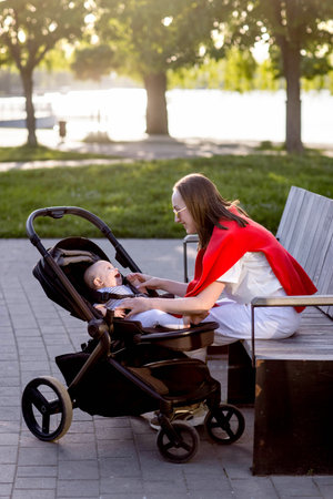 Young mother with her cute baby is sitting on a park bench.の写真素材