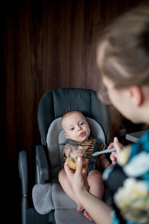 Mother feeding her son in a high chair. Baby's first complementary food.の写真素材