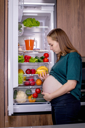 Pregnant woman takes a pear from the refrigerator.の写真素材
