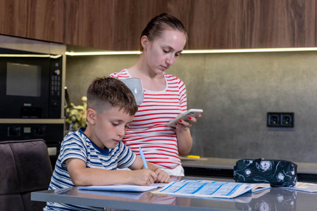 Mother helping her son doing homework in kitchen.の写真素材