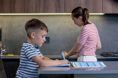Mother helping son with homework in kitchen at home.の写真素材