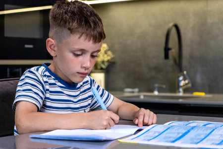 Schoolboy boy writes lessons in the kitchen.の写真素材