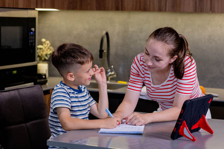 Beautiful mother helping son doing schoolwork at homeの写真素材