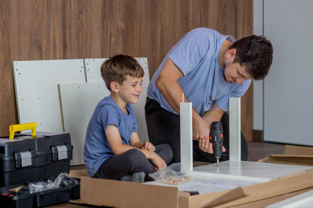 The son helps dad to collect furniture, nearby are tools and boards. Assembling furniture at homeの写真素材