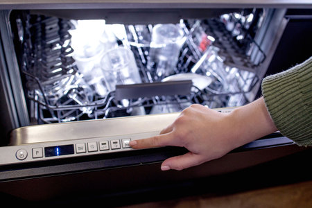 Womans hand turns on the dishwasher to wash the dishes. Built-in appliances in the kitchen.の写真素材