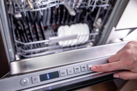 Woman's hand turns on the dishwasher to wash the dishes. Built-in appliances in the kitchenの写真素材