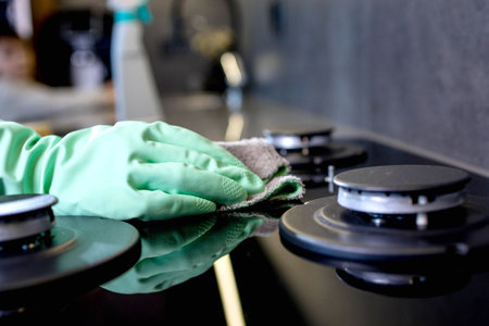 Hand in a green rubber glove washes the gas stove. Cleaning the kitchen.の写真素材