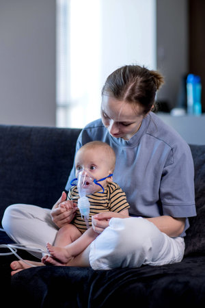 Woman with infant son makes inhalations using a nebulizer at home.の写真素材