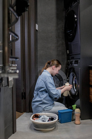 Young woman throws conditioner in granules into the washing machine.の写真素材