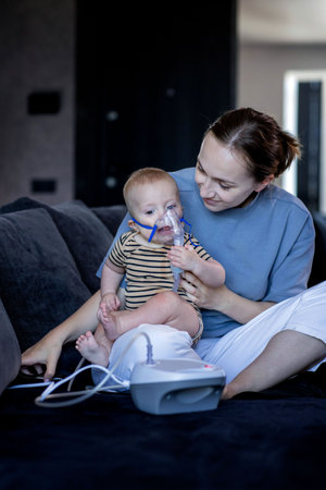 Woman with infant son makes inhalations using a nebulizer at home.の写真素材