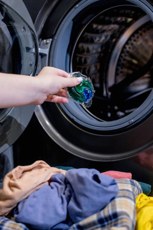 Woman putting laundry detergent capsule into washing machine indoors, closeup. Washing clothes.The concept of washing and cleanliness.の写真素材
