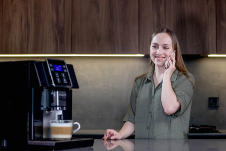 Coffee machine prepares coffee while the woman talking on the phone.の写真素材