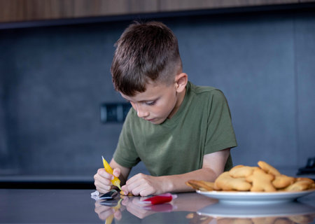 Cute boy decorating gingerbread cookies at home kitchen.の写真素材