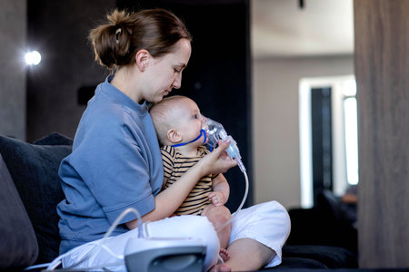 Woman with infant son makes inhalations using a nebulizer at home.の写真素材