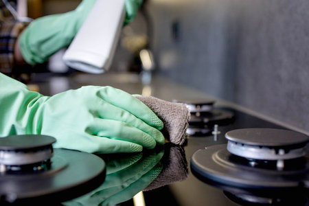 Hand in a green rubber glove washes the gas stove. Cleaning the kitchen.の写真素材