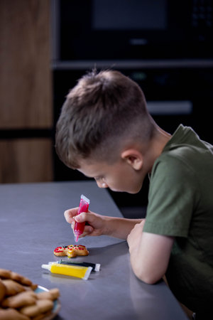 Cute boy decorating gingerbread cookies at home kitchen.の写真素材