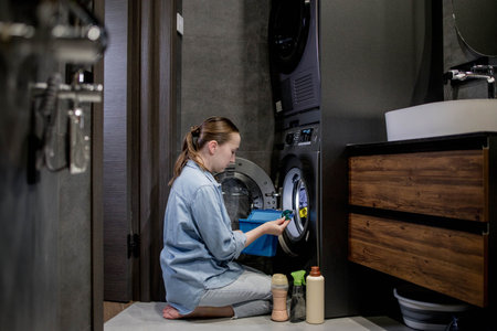 Woman putting laundry detergent capsule into washing machine indoors, closeup. Washing clothes.The concept of washing and cleanliness.の写真素材