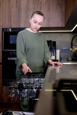 Young woman takes a glass out of the dishwasher in a modern kitchen.の写真素材