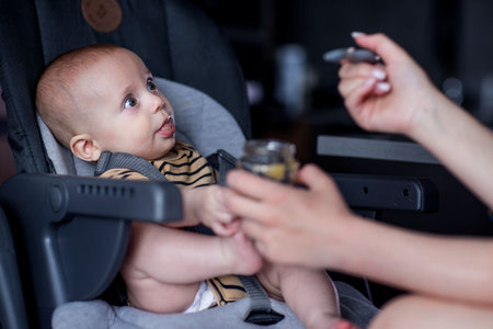 Mother feeding her baby with a spoon in the car seat at homeの写真素材