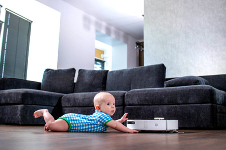 Baby boy looks at the robot vacuum cleaner with admiration and surpriseの写真素材