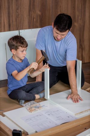 The son helps dad to collect furniture, nearby are tools and boards. Assembling furniture at homeの写真素材