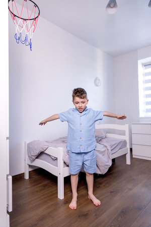 A young boy dressed in bright blue pajamas is happily stretching on his cozy bed, enjoying his time in the bedroomの写真素材