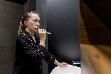 A woman in comfy pajamas brushes her teeth in a modern bathroom, enjoying her daily selfcare routine.の写真素材