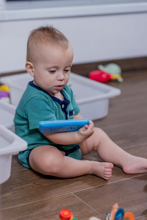 A small baby is happily sitting on the floor while engaging in play with a colorful toy phone, enjoying the experience of playtimeの写真素材