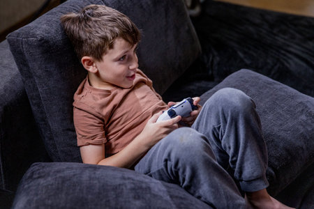 Boy is sitting on sofa at home and playing video games with his joypadの写真素材