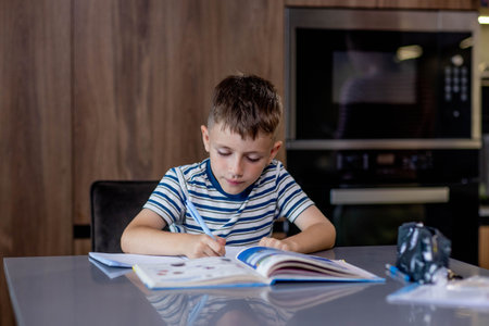 Schoolboy boy writes lessons in the kitchen.の写真素材
