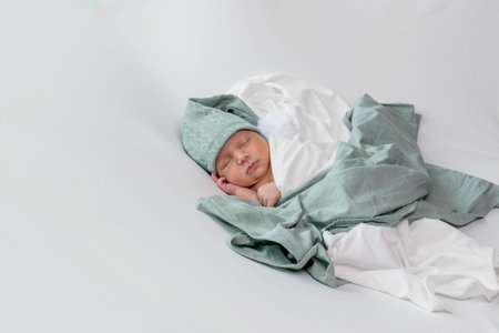 A precious newborn baby is gently swaddled in a soft, white blanket, providing warmth and comfort to the little one while they sleep peacefullyの写真素材