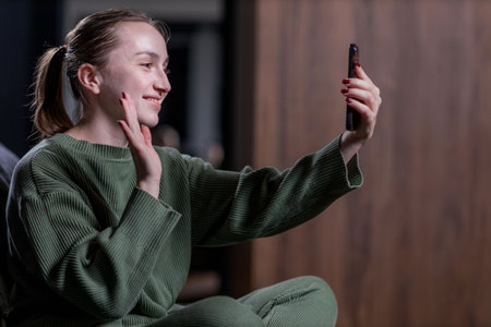 A woman in a green sweater takes a selfie with her phoneの写真素材